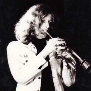 Black-and-white photo of a musician in a light jacket playing a trumpet on stage.