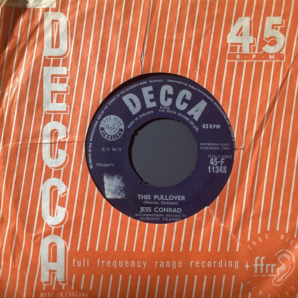 Close-up of an orange Decca Records box with a purple/black vinyl record partially visible in a circular cutout, showing '45') and track details.